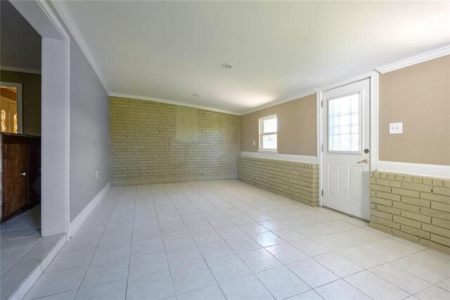 tiled spare room featuring crown molding and brick wall