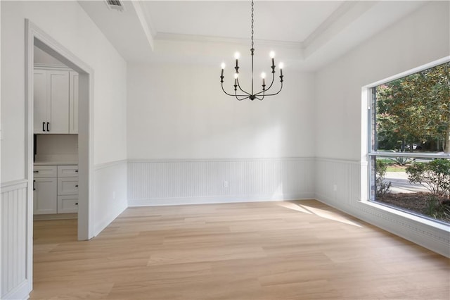 unfurnished dining area featuring visible vents, an inviting chandelier, wainscoting, light wood finished floors, and a raised ceiling