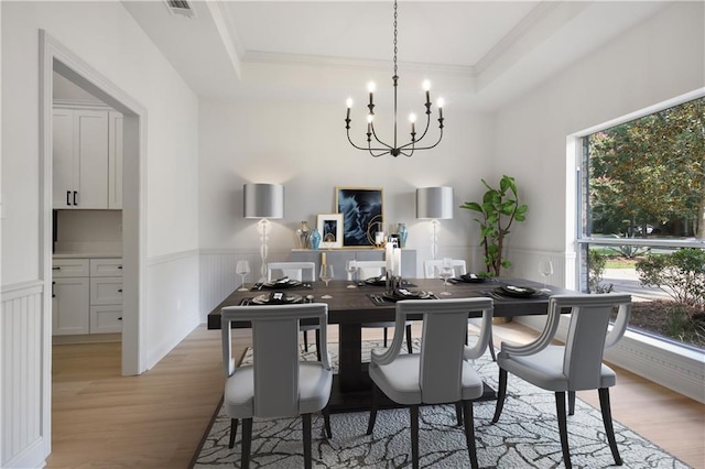 dining room with a tray ceiling, a chandelier, wainscoting, and light wood-style flooring