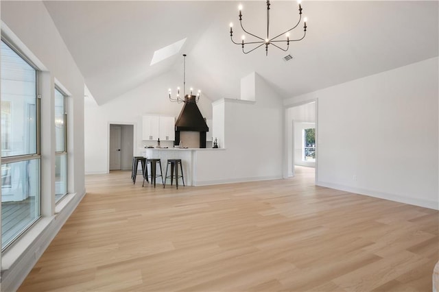 unfurnished living room featuring light wood-type flooring, a notable chandelier, a skylight, and high vaulted ceiling