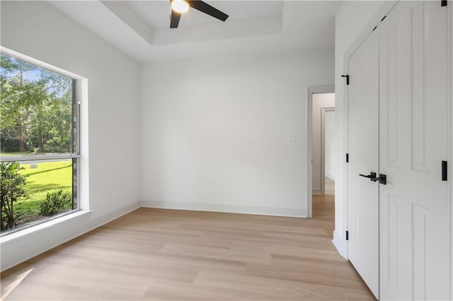 spare room featuring a tray ceiling, light wood-style flooring, a ceiling fan, and baseboards