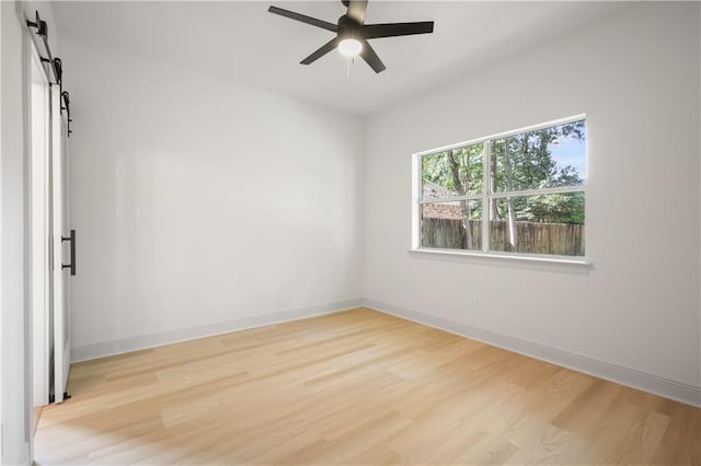 unfurnished room with a barn door, baseboards, light wood-style floors, and ceiling fan