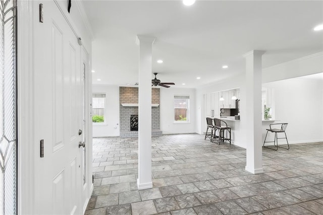 foyer featuring decorative columns, a brick fireplace, ceiling fan, and ornamental molding