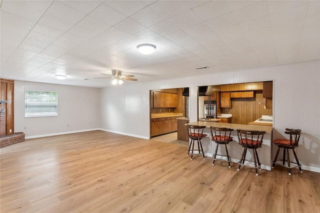 kitchen featuring ceiling fan, kitchen peninsula, light hardwood / wood-style floors, and a breakfast bar area