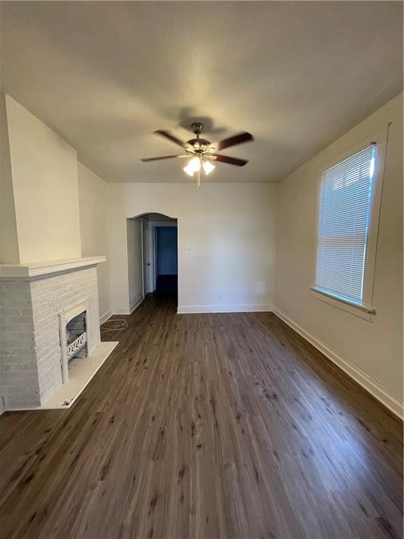 unfurnished living room with a brick fireplace, dark wood-type flooring, and ceiling fan