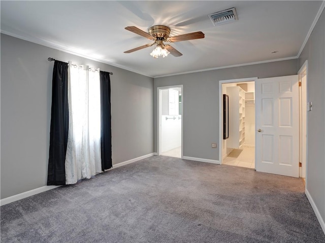 unfurnished bedroom featuring a walk in closet, ornamental molding, tile flooring, ensuite bath, and ceiling fan