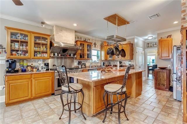 kitchen with crown molding, stainless steel appliances, a kitchen island with sink, light tile floors, and a breakfast bar area