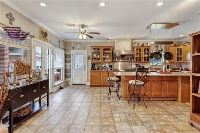 kitchen featuring wall chimney range hood, ceiling fan, crown molding, and light tile floors