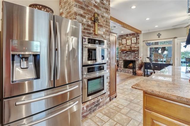 kitchen with brick wall, a fireplace, stainless steel appliances, ceiling fan, and light stone countertops