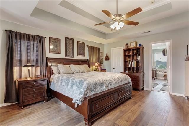 bedroom with ceiling fan, a tray ceiling, hardwood / wood-style floors, and ensuite bathroom