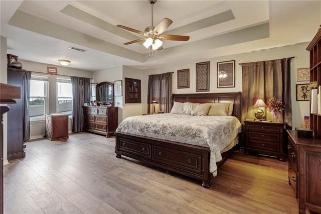 bedroom featuring ceiling fan, light hardwood / wood-style flooring, and a raised ceiling