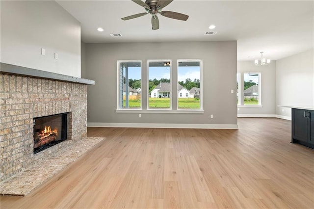 unfurnished living room with a brick fireplace, ceiling fan with notable chandelier, and light hardwood / wood-style floors