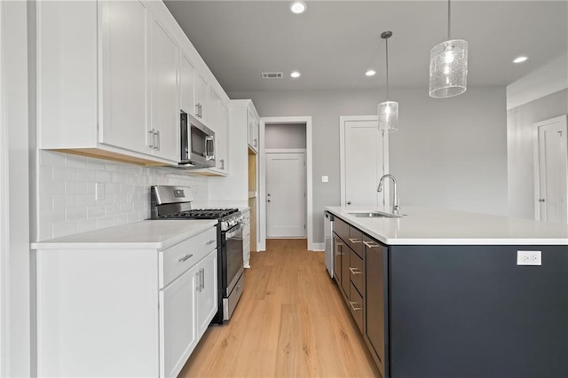 kitchen with sink, hanging light fixtures, white cabinets, and appliances with stainless steel finishes