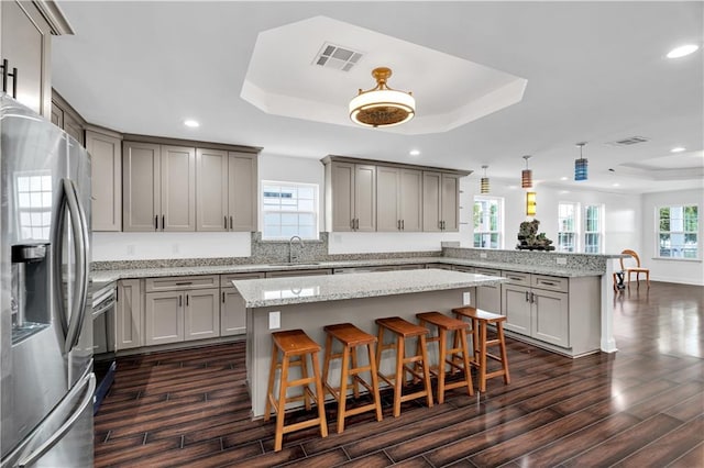 kitchen featuring a kitchen bar, kitchen peninsula, a tray ceiling, and stainless steel refrigerator with ice dispenser