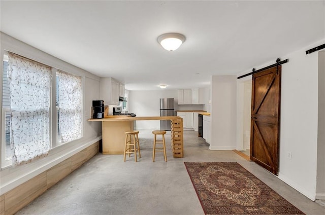 kitchen with stainless steel refrigerator, black dishwasher, white cabinets, a kitchen bar, and a barn door