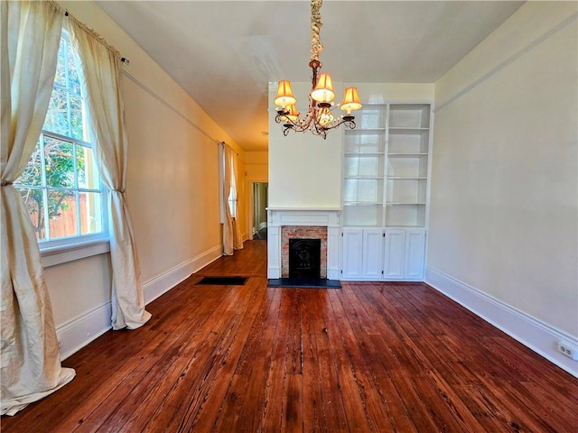 unfurnished living room featuring dark wood-type flooring, a fireplace, and a notable chandelier