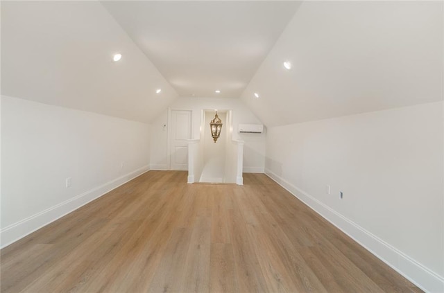 additional living space featuring lofted ceiling, a wall mounted air conditioner, and light hardwood / wood-style flooring