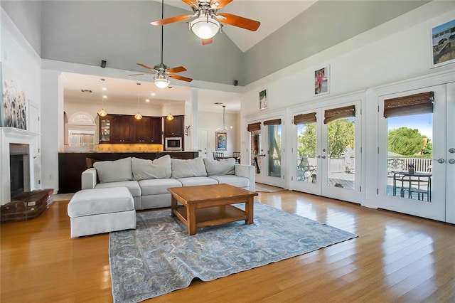 living room featuring high vaulted ceiling, french doors, a brick fireplace, ceiling fan, and light wood-type flooring