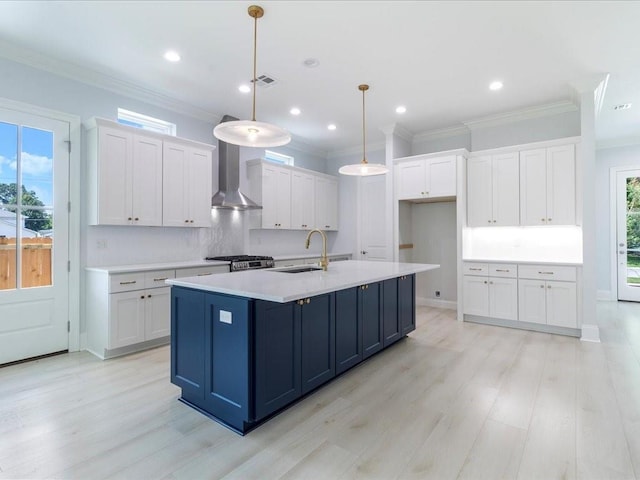 kitchen with pendant lighting, white cabinets, wall chimney range hood, and a center island with sink