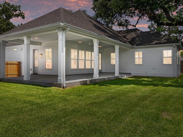 back house at dusk with a yard and ceiling fan