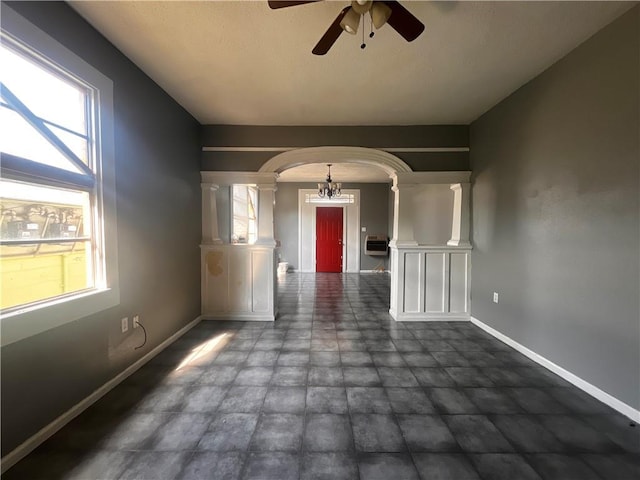 empty room with decorative columns and ceiling fan with notable chandelier