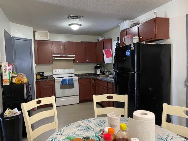 kitchen featuring light tile patterned floors, black fridge, white electric range oven, and a textured ceiling