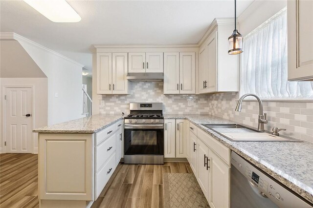 kitchen featuring appliances with stainless steel finishes, kitchen peninsula, hanging light fixtures, light hardwood / wood-style floors, and ornamental molding