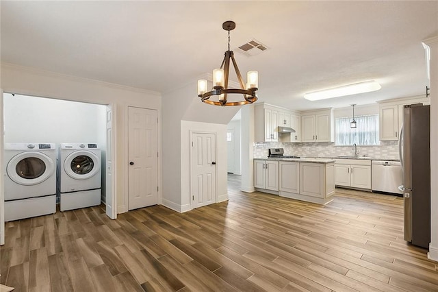 washroom featuring a chandelier, ornamental molding, sink, light hardwood / wood-style floors, and independent washer and dryer