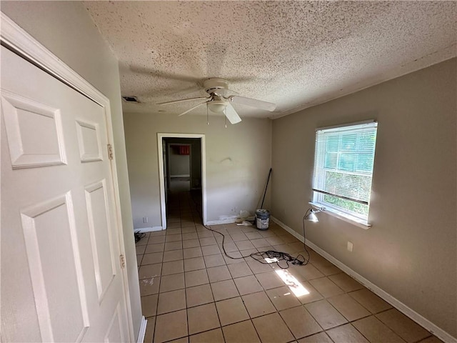 spare room featuring ceiling fan, light tile patterned floors, and a textured ceiling