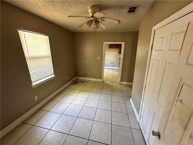 tiled empty room with ceiling fan and a textured ceiling