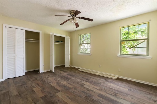 unfurnished bedroom with multiple closets, ceiling fan, dark hardwood / wood-style floors, and a textured ceiling