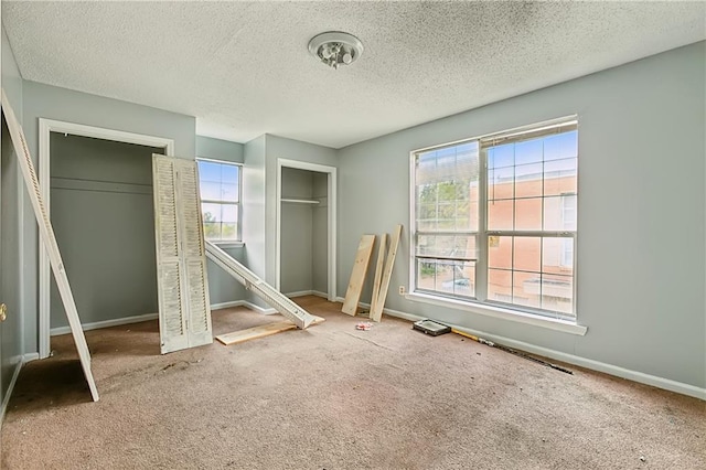 unfurnished bedroom with multiple closets, carpet, and a textured ceiling