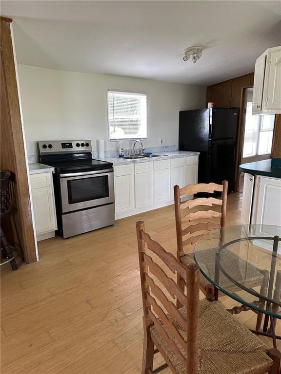 kitchen with sink, stainless steel electric stove, black refrigerator, light hardwood / wood-style flooring, and white cabinets