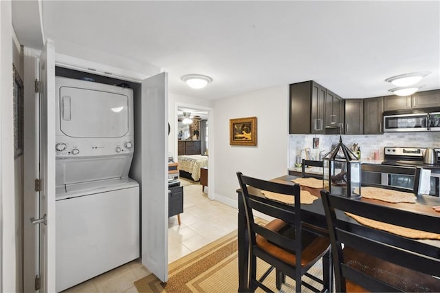 kitchen featuring light tile patterned floors, appliances with stainless steel finishes, backsplash, dark brown cabinets, and stacked washer / drying machine