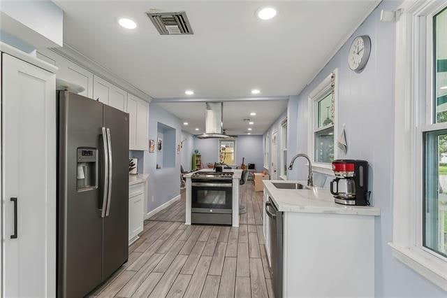 kitchen with island exhaust hood, stainless steel appliances, sink, light hardwood / wood-style floors, and white cabinets