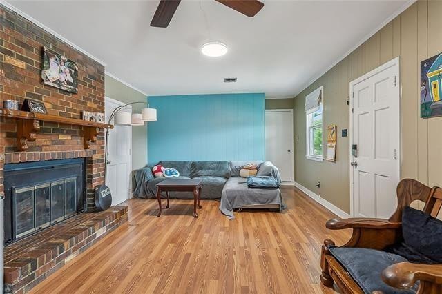 living room featuring ornamental molding, ceiling fan, a brick fireplace, and light hardwood / wood-style flooring