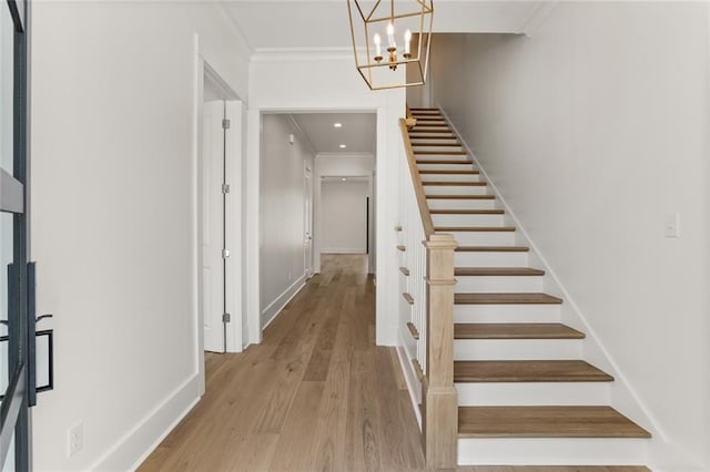 stairs featuring hardwood / wood-style floors, crown molding, and a chandelier