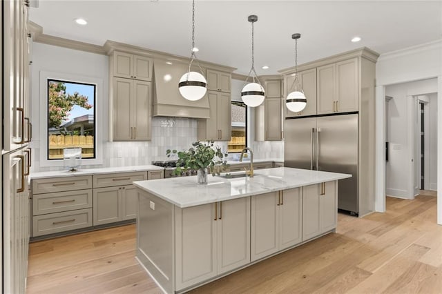 kitchen with built in fridge, a center island with sink, light stone countertops, and sink