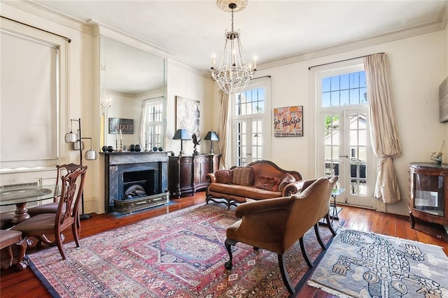 living room featuring french doors, wood-type flooring, crown molding, and a notable chandelier