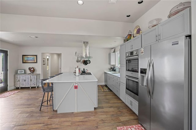 kitchen featuring appliances with stainless steel finishes, extractor fan, sink, a kitchen island, and wood-type flooring