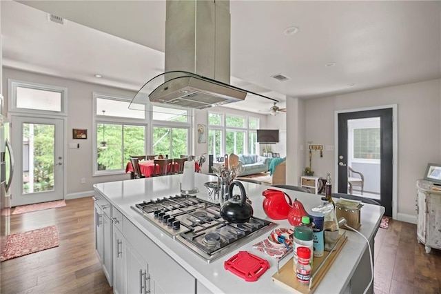 kitchen featuring stainless steel gas stovetop, a kitchen island, island exhaust hood, white cabinetry, and dark hardwood / wood-style flooring