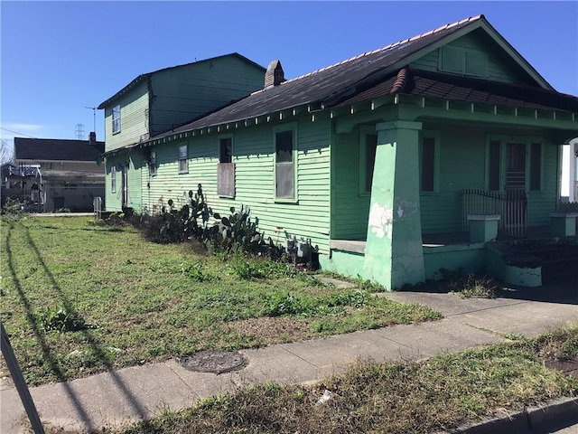 view of side of home featuring a porch, a yard, and a chimney