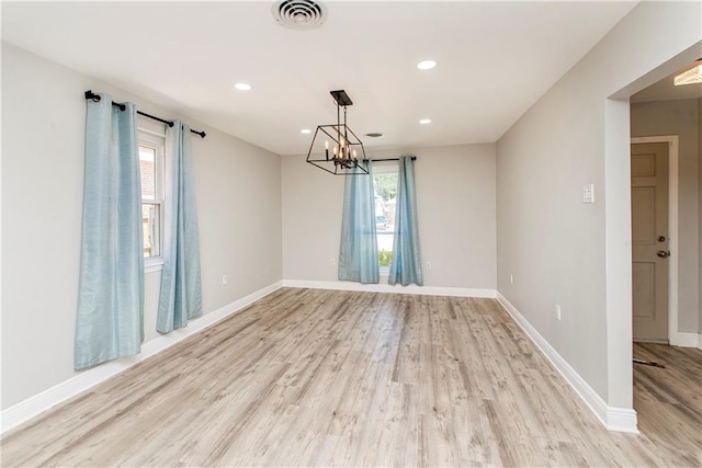 spare room featuring a notable chandelier and light hardwood / wood-style flooring