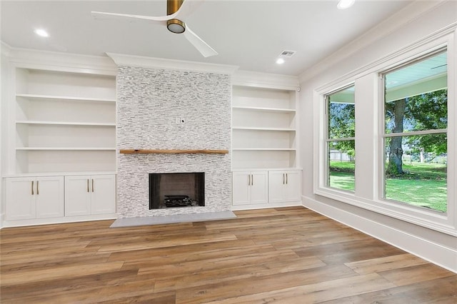 unfurnished living room featuring crown molding, ceiling fan, built in features, a fireplace, and light hardwood / wood-style floors