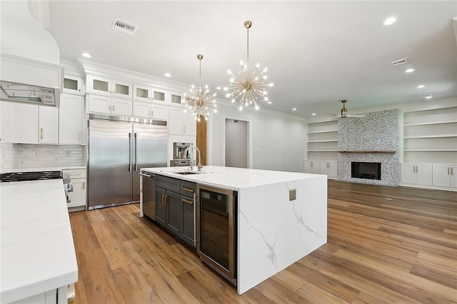 kitchen featuring stainless steel appliances, a kitchen island with sink, beverage cooler, white cabinets, and a stone fireplace