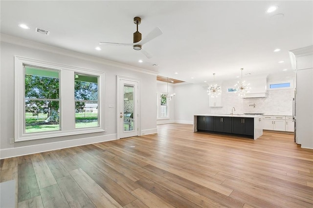 unfurnished living room featuring ceiling fan with notable chandelier, light hardwood / wood-style floors, ornamental molding, and sink