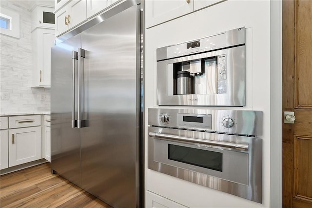 kitchen with white cabinets, light hardwood / wood-style flooring, stainless steel appliances, and tasteful backsplash