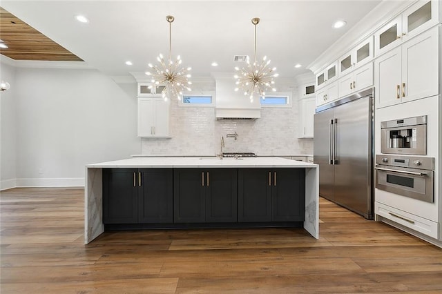 kitchen featuring a center island with sink, white cabinets, dark hardwood / wood-style floors, appliances with stainless steel finishes, and a notable chandelier