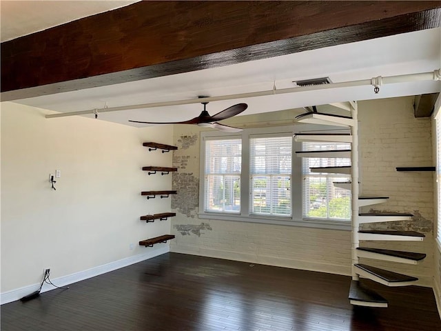 empty room with dark wood-type flooring, ceiling fan, brick wall, and beamed ceiling