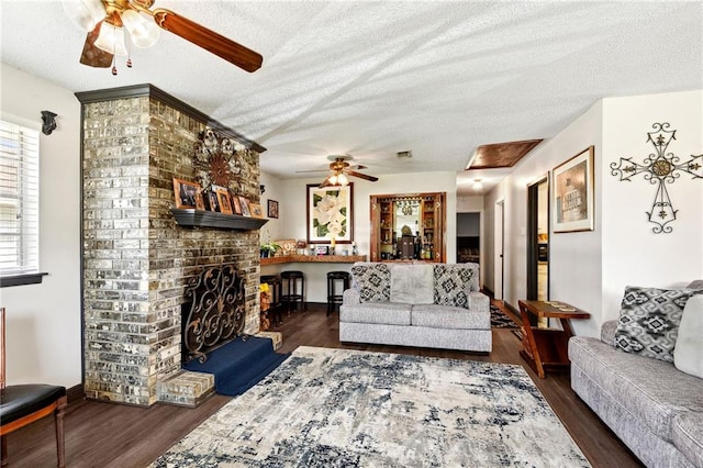 living room featuring a textured ceiling, dark hardwood / wood-style flooring, a brick fireplace, and ceiling fan